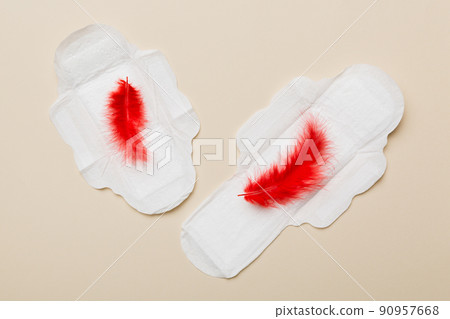 Women hygiene products or Sanitary pad with red feather on colored background. Pastel color. Closeup. Empty place for text. Female daily hygiene 90957668
