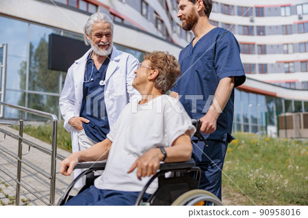 Nurse and doctor talking to patient on wheelchair in hospital yard during walk 90958016
