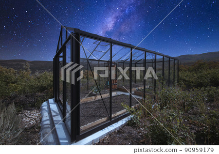 Glass greenhouse in the middle of a shrubland under the starry composite milky way sky 90959179