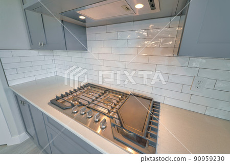 Kitchen with cooktop stove and exhaust hood against white tile backsplash wall 90959230
