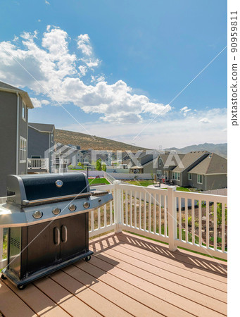 Vertical White puffy clouds Wooden deck of a house with a barbecue grill and a view of residential houses and mountain Vertical White puffy clouds Wooden deck of a house with a barbecue grill and a view of residential houses and mountain 90959811