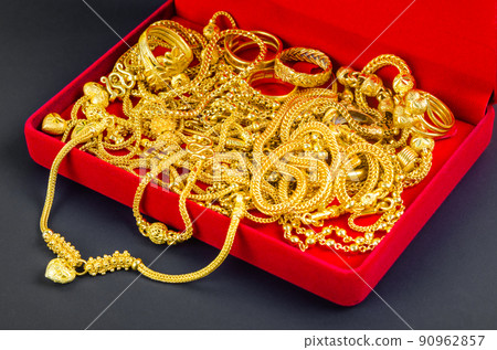 Many gold necklaces in a red velvet box on red background. 90962857