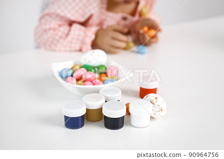 Girl painting Easter eggs and preparing for Easter day. Side view of easter eggs at white table, paints in jars. Girl painting an Easter decoration. Girl painting Easter eggs and preparing for Easter day. Side view of easter eggs at white table, paints in jars. Girl painting an Easter decoration. 90964756