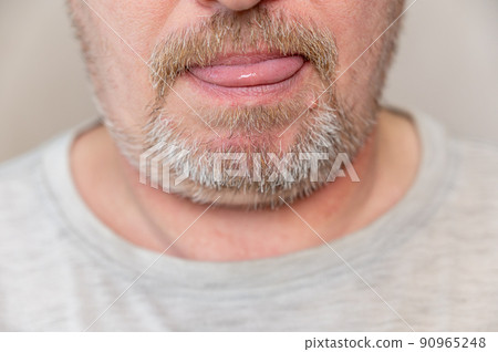 The lower part of a man's face. A mature man with stubble stuck out his tongue. Gray hair on beard and mustache. Man wriggling in front of camera. Close-up. Selective focus. 90965248