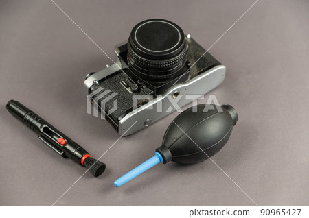Repair and service of photographic equipment concept. Set of cleaning tools and camera against a gray background. Brush and dust blower. Film camera. Selective Focus. 90965427