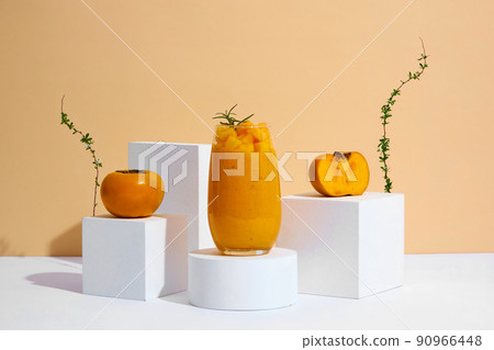 Front view of persimmon frappe with circle , square podium , flowers in trendy almond background for food advertising Front view of persimmon frappe with circle , square podium , flowers in trendy almond background for food advertising 90966448