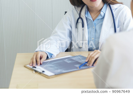 Two asian women doctors discuss meeting doctor's office medical clinic looking x-ray film consulting patient disease. Asian medical lab young women talking together discussing healthcare teamwork Two asian women doctors discuss meeting doctor's office medical clinic looking x-ray film consulting patient disease. Asian medical lab young women talking together discussing healthcare teamwork 90967649