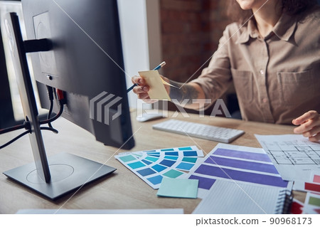 Cropped shot of female designer holding sticky note while using computer, working with color samples and blueprint project of new apartments Cropped shot of female designer holding sticky note while using computer, working with color samples and blueprint project of new apartments 90968173