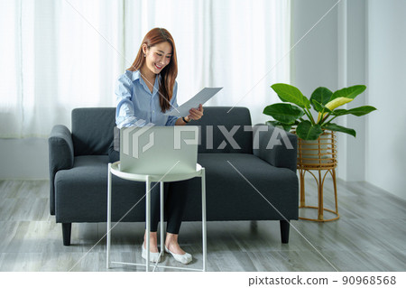 self employed, business owner, pleasure from work, portrait of Asian woman using computer holding financial documents to check or plan budget, manage investment risk at home. 90968568
