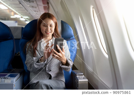Travel and technology. Young asian woman in plane using smartphone while sitting in airplane seat 90975861