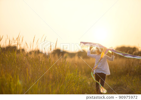 A girl runs into a field with a kite, learns to launch it. Outdoor entertainment in summer, nature and fresh air. Childhood, freedom and carelessness. A child with wings is a dream and a hope. A girl runs into a field with a kite, learns to launch it. Outdoor entertainment in summer, nature and fresh air. Childhood, freedom and carelessness. A child with wings is a dream and a hope. 90975972
