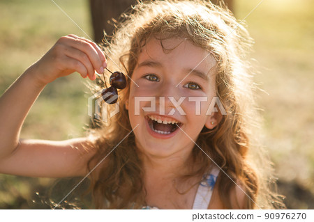 A cheerful sweet girl with cherry berries in her mouth. Funny summer portrait of a child with a cherry, gifts of summer, summer time. 90976270