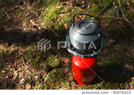 Cooking, heating a tourist kettle on a portable gas burner with a red gas cylinder. Camping, a man cooks breakfast outdoors. Summer outdoor activities 90976428