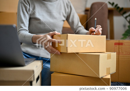 Female online shopping store owner packing a delivery box, writing a customer address Female online shopping store owner packing a delivery box, writing a customer address 90977006