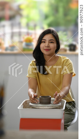 Happy young woman making ceramic pot from clay in pottery workshop. Activity, handicraft, hobbies concept 90977623