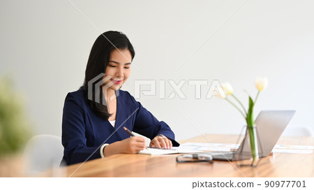 Charming young business entrepreneur sitting at her spacious office and working with financial document Charming young business entrepreneur sitting at her spacious office and working with financial document 90977701