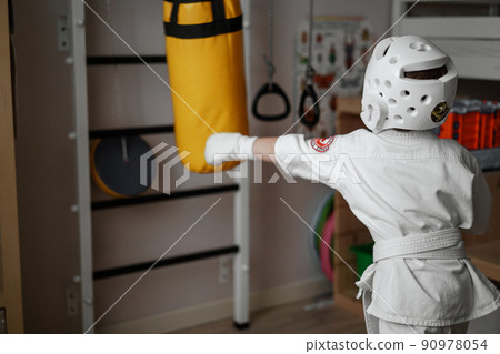 little boy in kimono and helmet training at home punching a punchbag 90978054