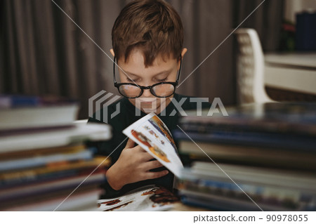 cute caucasian boy wearing glasses reading a book. Cheerful boy peeking from behind piles of books 90978055