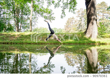Young woman doing sun salutation yoga practice on grass in park near river Young woman doing sun salutation yoga practice on grass in park near river 90978361