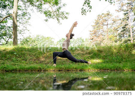 Young woman doing sun salutation yoga practice on green grass loan in sunny park Young woman doing sun salutation yoga practice on green grass loan in sunny park 90978375