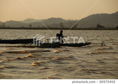 Sunset silhouettes of a fisherman among the boats in Lak Lake in the township of Lien son, Dak Lak Vietnam Sunset silhouettes of a fisherman among the boats in Lak Lake in the township of Lien son, Dak Lak Vietnam 90978408