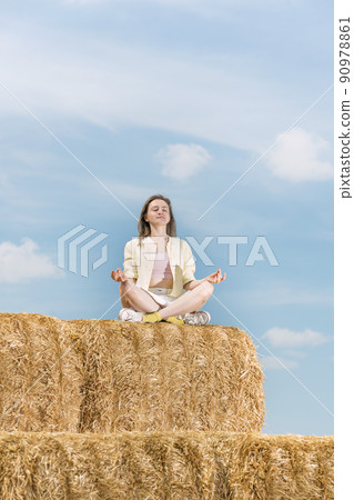 Young woman sits in lotus position on huge haystack and meditates. Countryside holiday. 90978861
