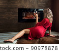 Woman sitting by fireplace with glass of wine 90978878