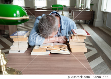 Senior man falls asleep over a textbook, he is sitting at a table Senior man falls asleep over a textbook, he is sitting at a table 90981366