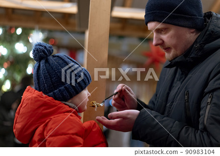 caucasian man, father of little daughter feeding little girl at christmas market caucasian man, father of little daughter feeding little girl at christmas market 90983104