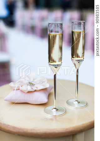 Two glasses and pink pillow with wedding rings on the table 90983585