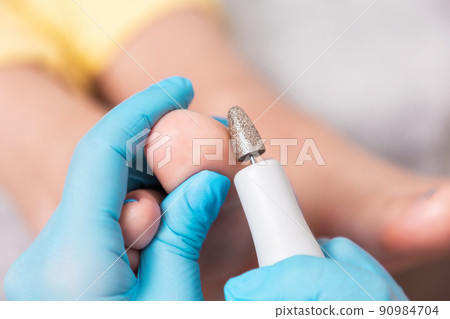 A pedicurist does a hardware peeling of the skin of the toes. Close-up. The concept of professional podology and chiropody 90984704