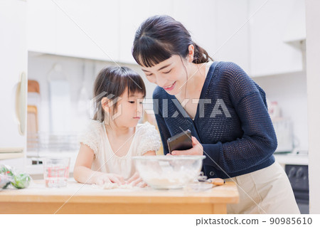 女兒一邊做飯一邊和媽媽和智能手機一起看食譜 90985610