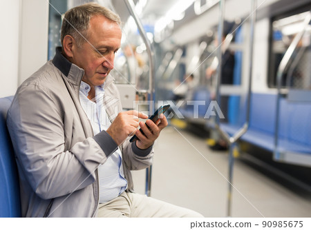 Elderly passenger is engrossed in information on smartphone while traveling in subway car 90985675
