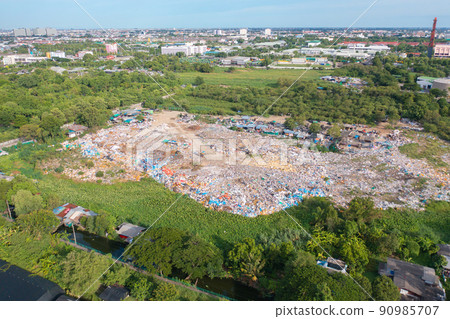 Aerial view of stack of different types of large garbage pile, plastic bags, and trash with a tractor car in industrial factory in environmental pollution. Waste disposal in dumping site. Aerial view of stack of different types of large garbage pile, plastic bags, and trash with a tractor car in industrial factory in environmental pollution. Waste disposal in dumping site. 90985707
