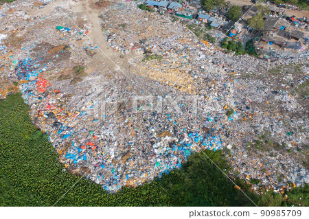 Aerial view of stack of different types of large garbage pile, plastic bags, and trash with a tractor car in industrial factory in environmental pollution. Waste disposal in dumping site. 90985709
