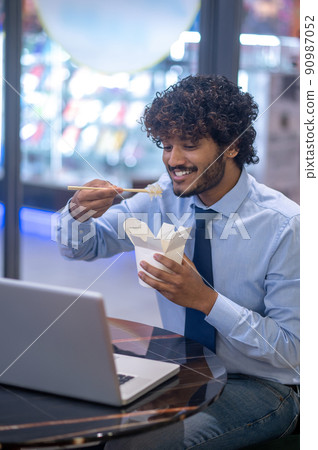 Happy man eating looking at laptop at workplace Happy man eating looking at laptop at workplace 90987052