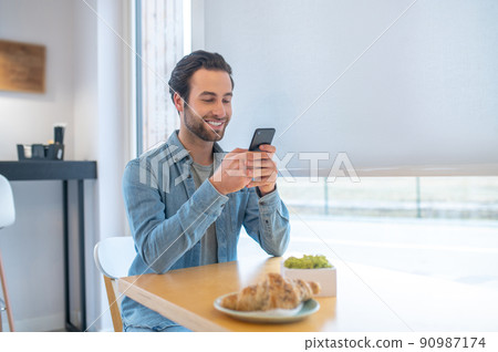 Smiling man looking at smartphone sitting in cafe 90987174
