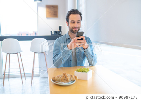 Man looking at smartphone sitting at table 90987175