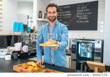 Man holding out croissant on plate to camera 90987176