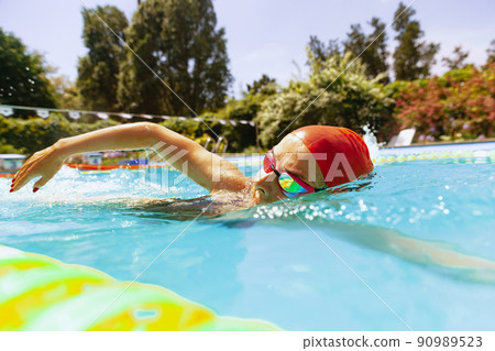 At swimming pool. Sportive woman, swimmer in swimming cap and goggles training at open public pool. Vacation, active lifestyle, power, energy, sports movement concept. 90989523