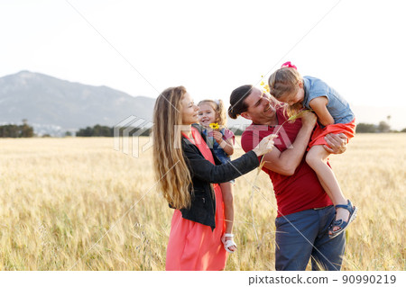 Happy family father of mother and two daughters sisters on nature at sunset.Carefree parents having fun with their kids on a field. Happy family father of mother and two daughters sisters on nature at sunset.Carefree parents having fun with their kids on a field. 90990219