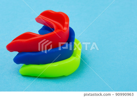three boxing mouth guards in blue, red and green, lie one on top of the other 90990963