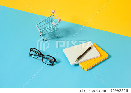 Smartphone, stationery, glasses and shopping cart over blue table. Smartphone, stationery, glasses and shopping cart over blue table. 90992206