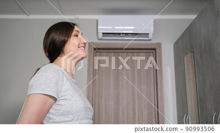 Woman turns on air conditioner with remote control at heat Woman turns on air conditioner with remote control at heat 90993506