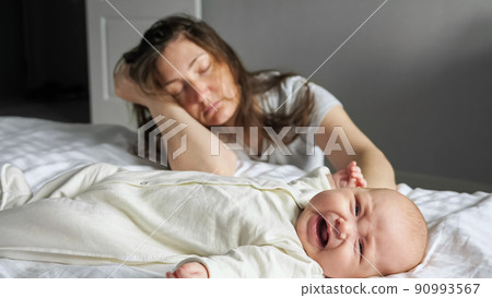 Tired mother sleeps sitting on floor near crying baby girl Tired mother sleeps sitting on floor near crying baby girl 90993567