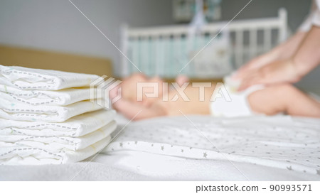 Mother hands dress baby in new diaper on blurred background Mother hands dress baby in new diaper on blurred background 90993571