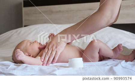 Mother smears cream on soft skin of newborn baby on bed Mother smears cream on soft skin of newborn baby on bed 90993574