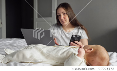 Busy mother works at home looking after little baby girl Busy mother works at home looking after little baby girl 90993578