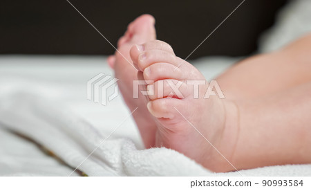 Barefoot newborn girl lies on white sheet making moves Barefoot newborn girl lies on white sheet making moves 90993584