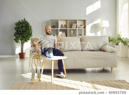 Man with leg injury uses mobile phone to communicate online with friends or browse social networks. 90993789